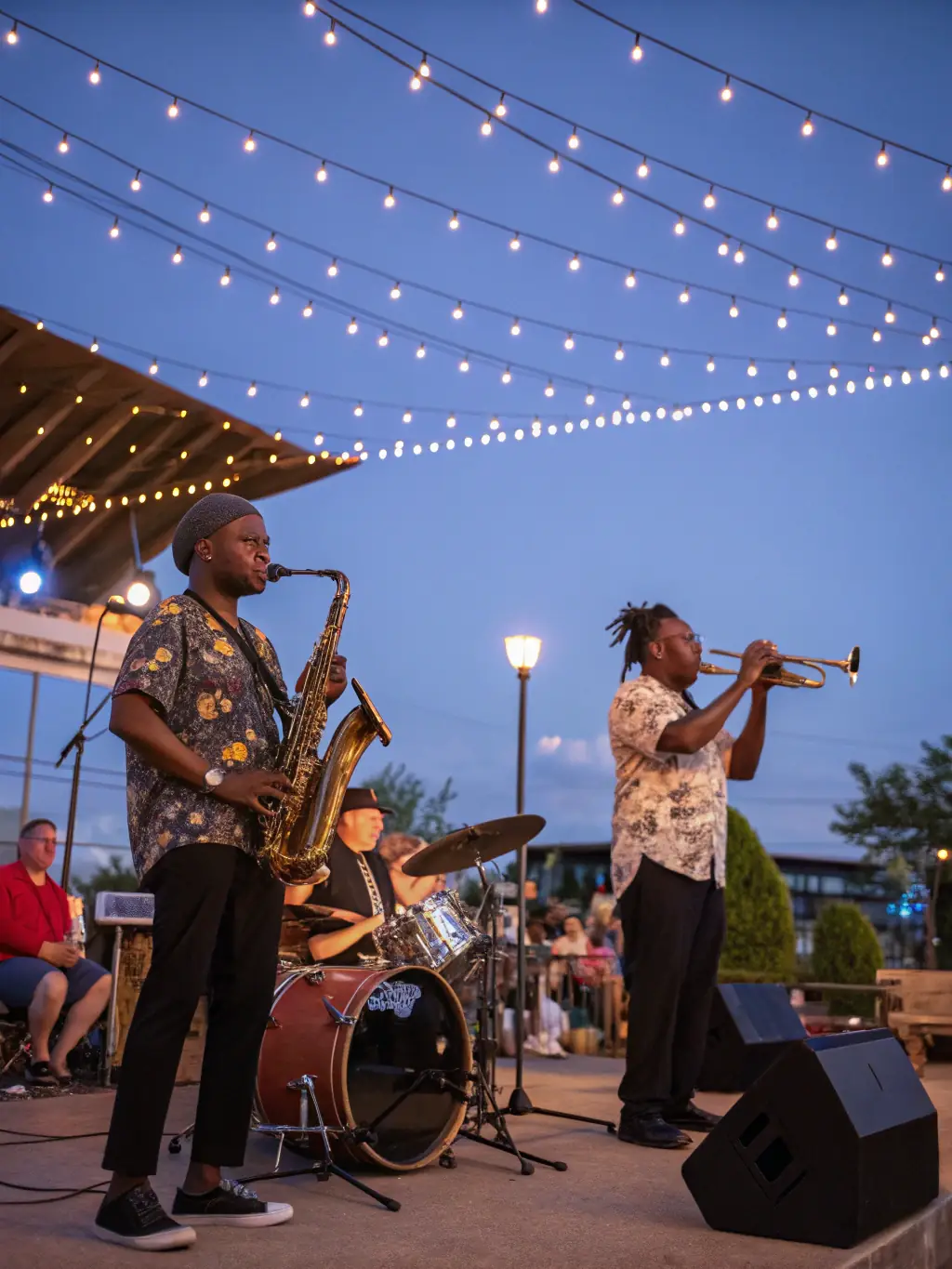 A photo of a jazz ensemble performing in a cozy village square, with people gathered around tables enjoying food and drinks.